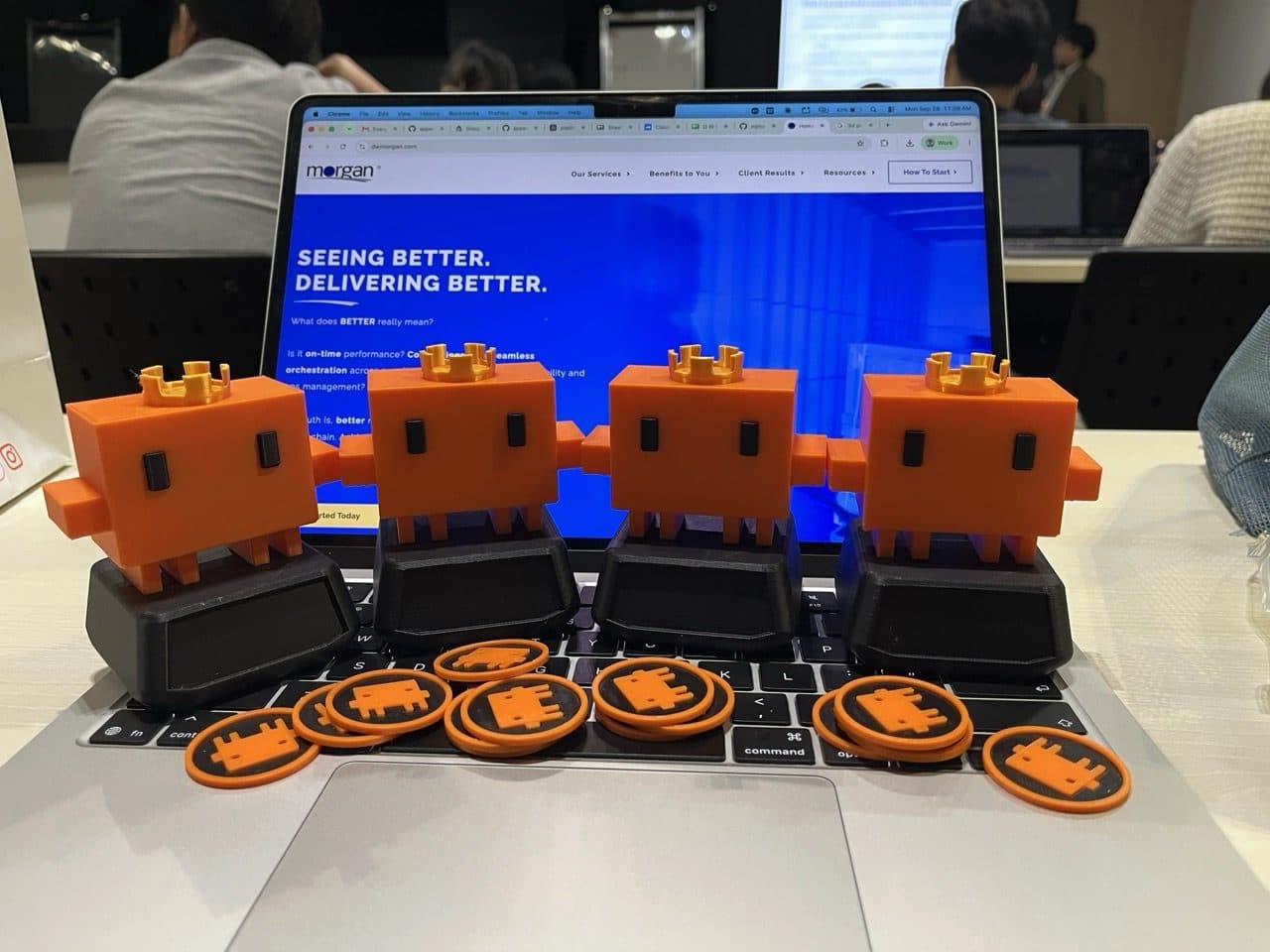Four orange pixel-robot trophies wearing gold crowns, with commemorative tokens, on a laptop showing the D.W. Morgan website