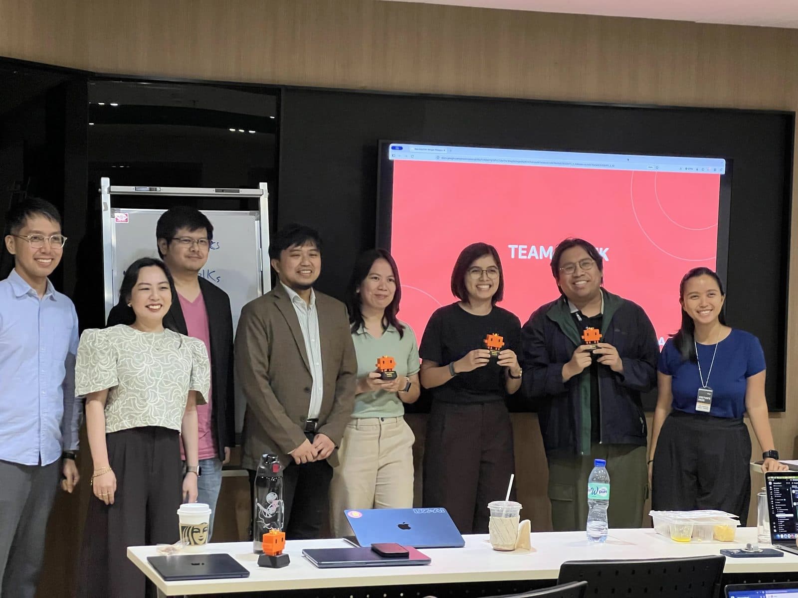 Eight members of the D.W. Morgan team and Apper AI Solutions smiling for a group photo, three of them holding orange pixel-robot trophies